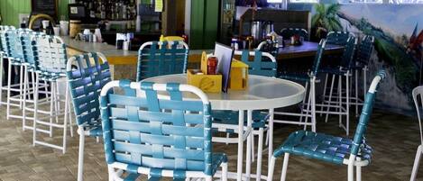A restaurant with blue and white chairs, a round table, and a bar area in the background.