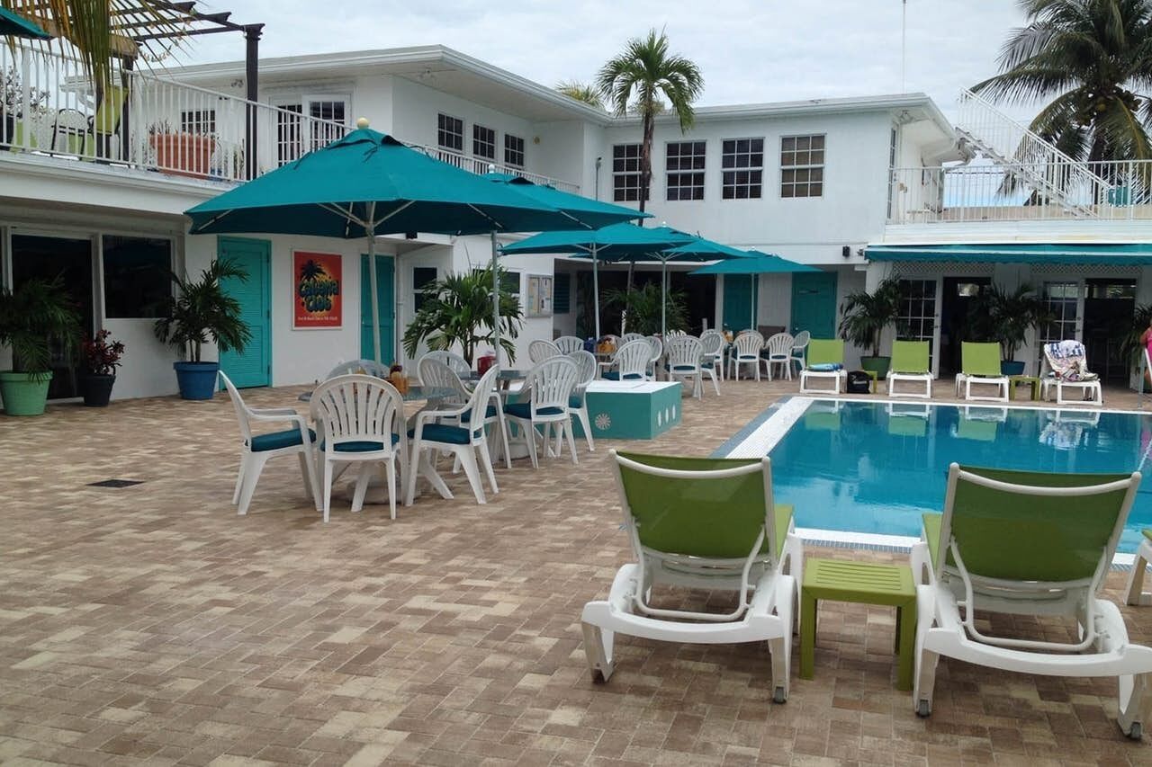 A pool area with white lounge chairs and green cushions, surrounded by a white building with multiple windows and a balcony.