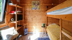 Interior de una cabaña de madera con una cama litera, una estantería, una mesita y una ventana.
