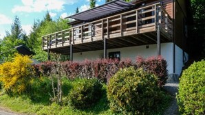 Un edificio de dos plantas con un balcón, rodeado de abundante vegetación y árboles.