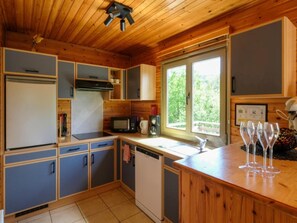 A kitchen with wooden cabinets, a microwave, a sink, and a window with a view of greenery. - Holiday Home in Ardennes Near Hotton Caves (La Roche-en-Ardenne)