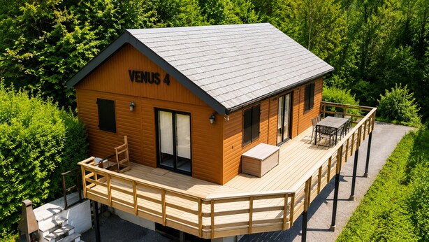 Una cabaña de madera llamada VENUS 4 con una terraza, un pequeño espacio de estar al aire libre y una escalera que lleva a la entrada.