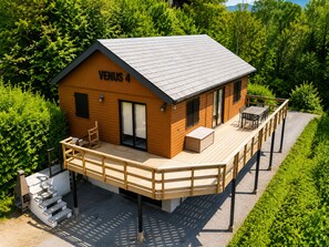 A wooden cabin named VENUS 4 with a deck, a small outdoor seating area, and a staircase leading to the entrance. - Holiday Home in Ardennes Near Hotton Caves (La Roche-en-Ardenne)