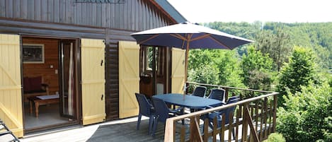 A wooden cabin with a deck, a table with chairs, and an umbrella.