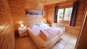 Une chambre à coucher dans une cabane en bois, avec un lit, des tables de chevet, une fenêtre avec des rideaux et un tableau accroché au mur.