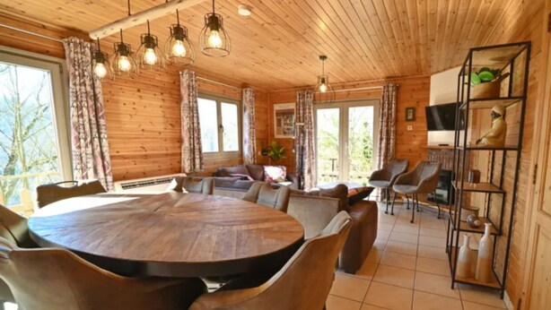 L’intérieur d’un chalet en bois comprend une table à manger ronde, plusieurs chaises, un canapé et un téléviseur posé sur une étagère.