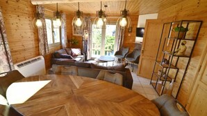 Un intérieur chaleureux avec des éléments en bois, une table de salle à manger ronde, un canapé en cuir et des luminaires suspendus.