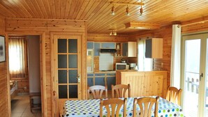 A wooden cabin with a dining area, kitchen, and a large window. - Holiday Home in La Roche With Sauna (La Roche-en-Ardenne)
