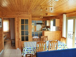 A wooden cabin with a dining area, kitchen, and a large window.