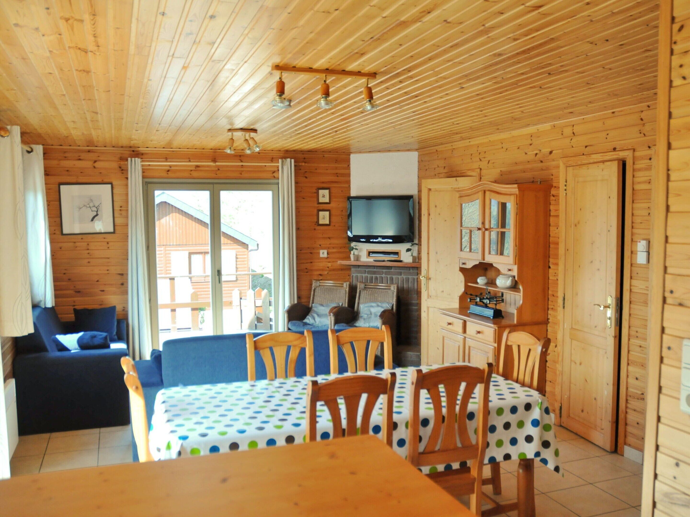 A wooden cabin interior with a dining area, a sofa, a television, and a fireplace.