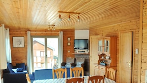 A wooden cabin interior with a dining area, a sofa, a television, and a fireplace. - Holiday Home in La Roche With Sauna (La Roche-en-Ardenne)