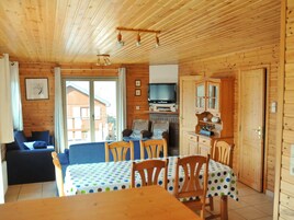 A wooden cabin interior with a dining area, a sofa, a television, and a fireplace.