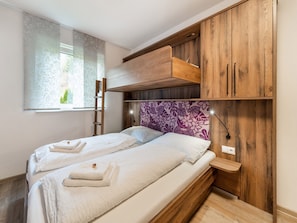 Ein Schlafzimmer mit zwei Betten, Holzschränken, einer Leiter und einem Fenster mit blumigen Vorhängen.