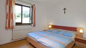 A bedroom with a bed, two bedside lamps, a window with curtains, a radiator, and a cross on the wall. - Apartment in Huttau Near Ski Amade Slopes (Huettau)