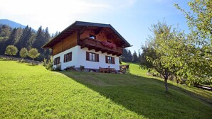 A two-story chalet with a wooden exterior and a balcony with flowers. - Apartment in Huttau Near Ski Amade Slopes (Huettau)