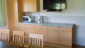A compact kitchen with wooden cabinets, a microwave, a coffee maker, and a flat-screen TV mounted on the wall. - Lush Holiday Home in Hüttau near Ski Area (Huettau)