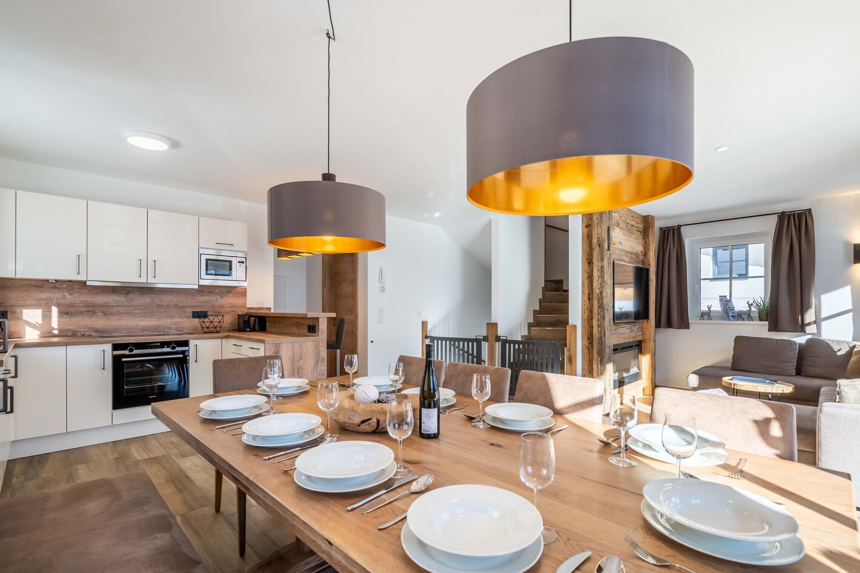 A modern kitchen with white cabinets and a wooden countertop, a dining area with a wooden table set for four, and a living area with a sofa and a TV.