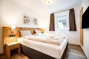 Habitació d'hotel amb llit, taules de nit, obra d'art a la paret, finestra amb cortines i televisió plana penjada a la paret.