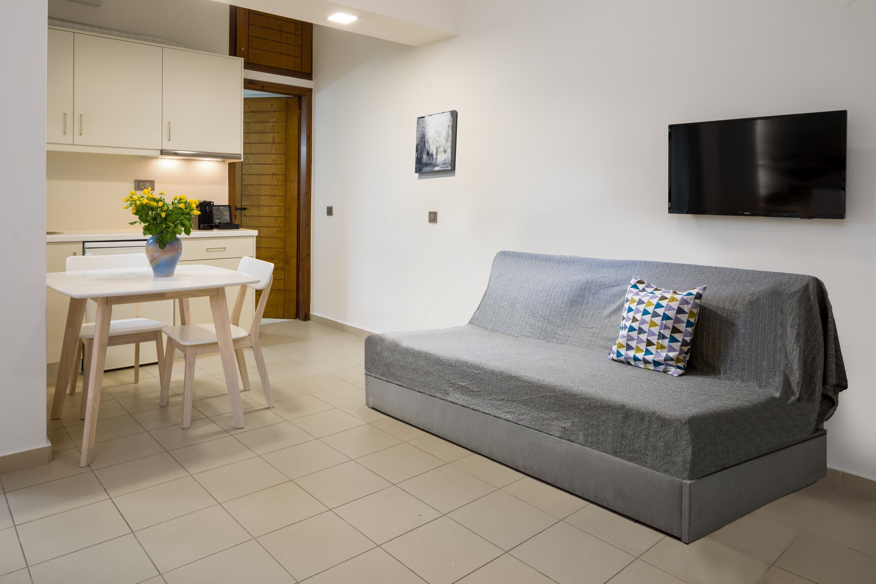 Un salon moderne avec un canapé gris, une petite table et un téléviseur fixé au mur.