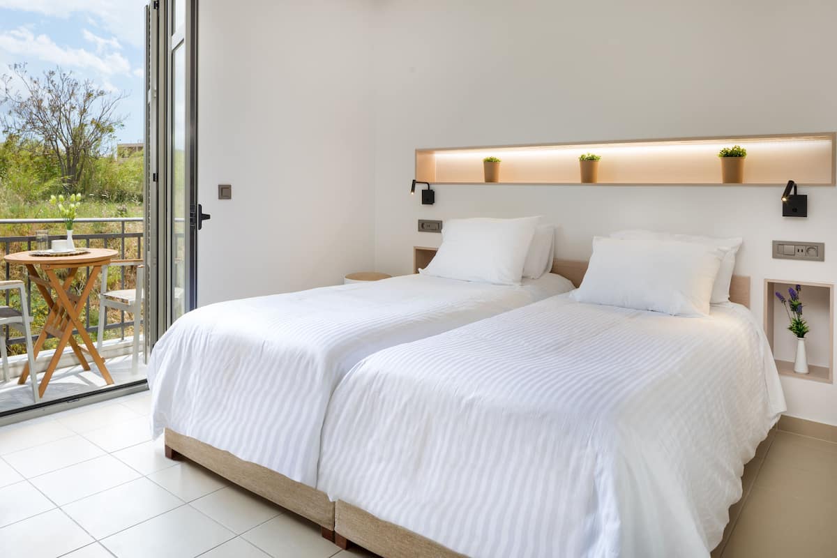 A double bed with white bedding, a small table with chairs, and a balcony with a view of trees.