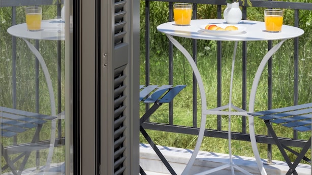 A balcony with a table set for breakfast, overlooking a scenic view of the sea and hills.