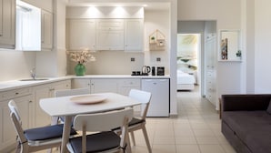 A modern kitchen with white cabinets, a dining table with chairs, a coffee machine, and a refrigerator.