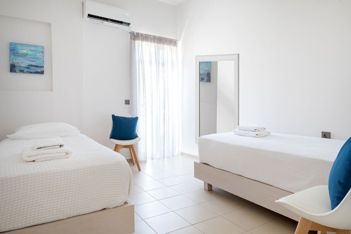 A modern hotel room with two beds, a chair, a mirror, and a painting on the wall.
