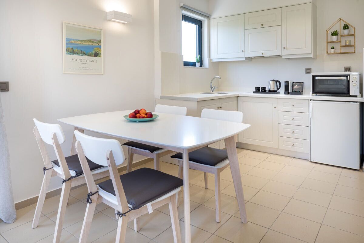 A modern kitchen with white cabinets, a white countertop, and a dining area with a white table and chairs.