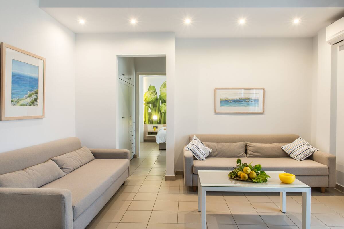A modern living room with two sofas, a coffee table with fruit, and artwork on the walls.