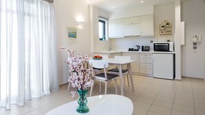 A modern kitchen with white cabinets, a microwave, and a sink. There is a dining area with a white table and chairs, and a vase with flowers on the table.