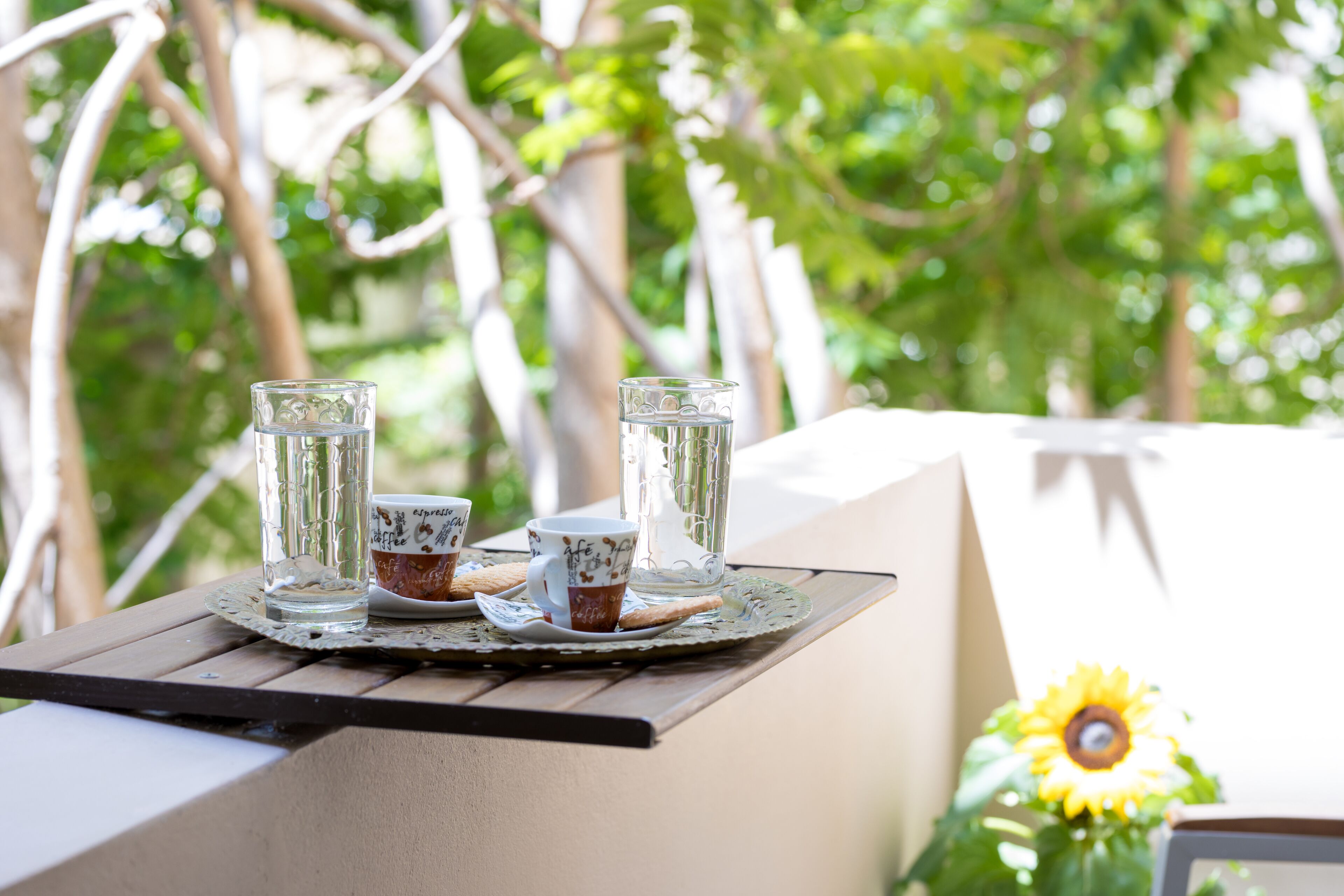 A table with two glasses of water, a cup, and a plate with a biscuit, set on a doily.
