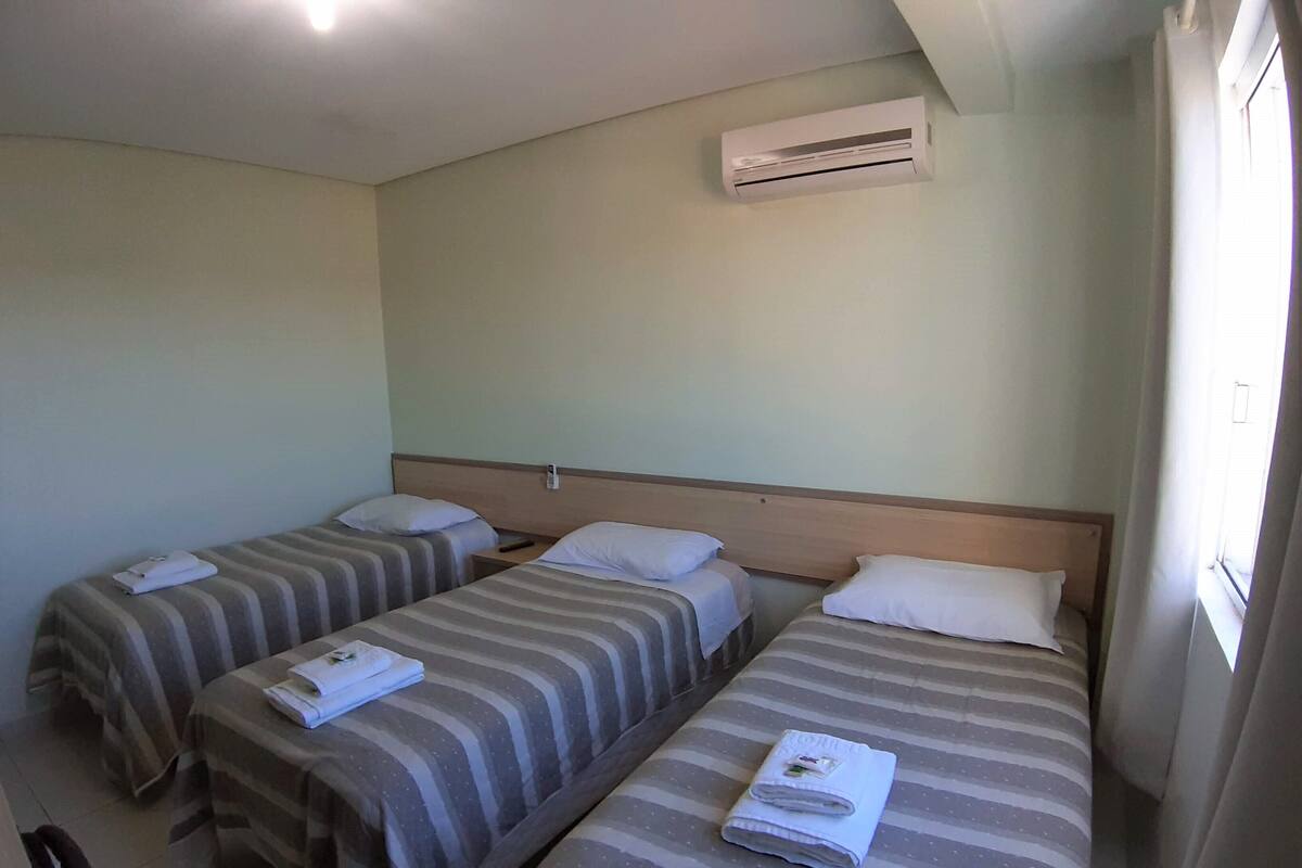 Ein Hotelzimmer mit zwei Einzelbetten, jeweils mit gestreifter Bettwäsche und einem gefalteten Handtuch. Eine Klimaanlage ist an der Wand über den Betten angebracht.