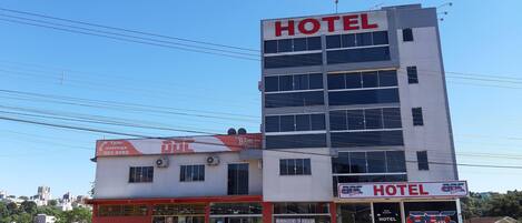 Un hotel con un llamativo letrero 'HOTEL' en la fachada, una visible entrada y coches aparcados delante.