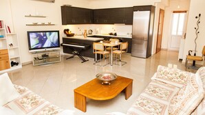 Una sala de estar moderna con un sofá, una mesa de centro, televisión y una cocina con armarios y un refrigerador.