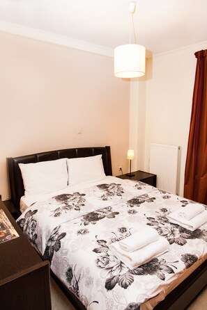 A neatly made bed with floral bedding, a bedside lamp, and a view of a radiator. - Spacious Apartment in Neos Kosmos (Athens)