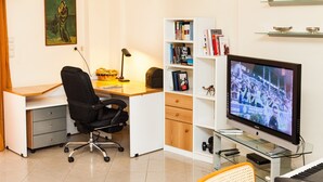 Un espacio de oficina moderno con un escritorio, una silla de oficina, una estantería, un televisor y un piano.