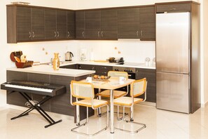 A modern kitchen with dark cabinets, a stainless steel refrigerator, a built-in keyboard, and a dining table with four chairs. - Spacious Apartment in Neos Kosmos (Athens)