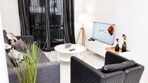 Una sala de estar moderna con un sofá gris, un sillón negro, una mesa redonda de centro y un televisor sobre un mueble.