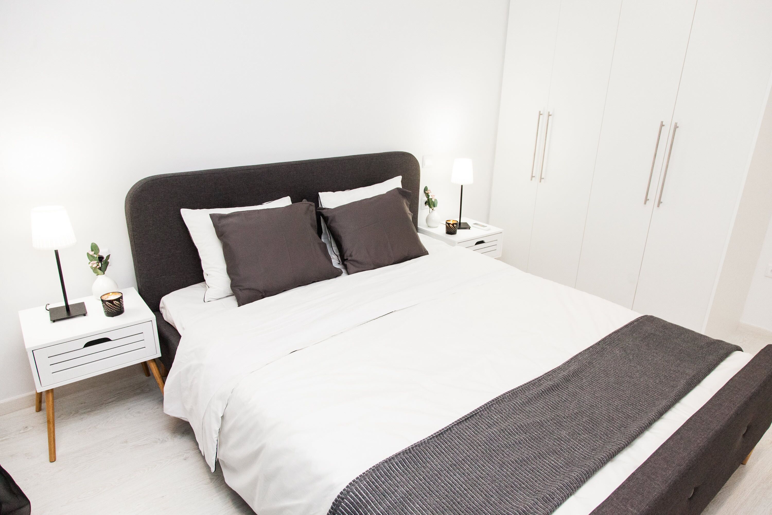 Quarto bem arrumado com cama, mesas de cabeceira e guarda-roupa.