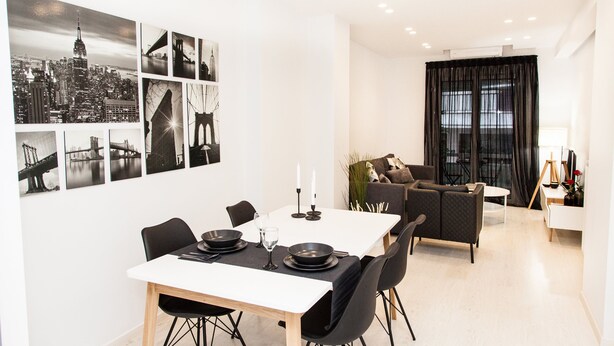Un comedor moderno con una mesa blanca para cuatro, sillas negras y un camino de mesa negro.