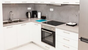 Una cocina moderna con armarios blancos, un lavamanos de acero inoxidable, horno empotrado y placa de inducción negra.