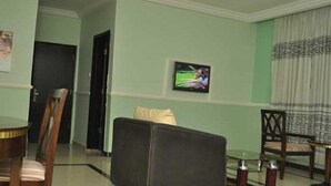 Una camera d'hotel con zona pranzo, TV a parete e finestra con tende.