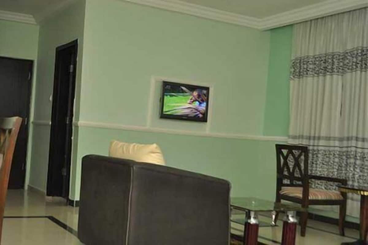 A hotel room with a dining area, a TV mounted on the wall, and a window with curtains.