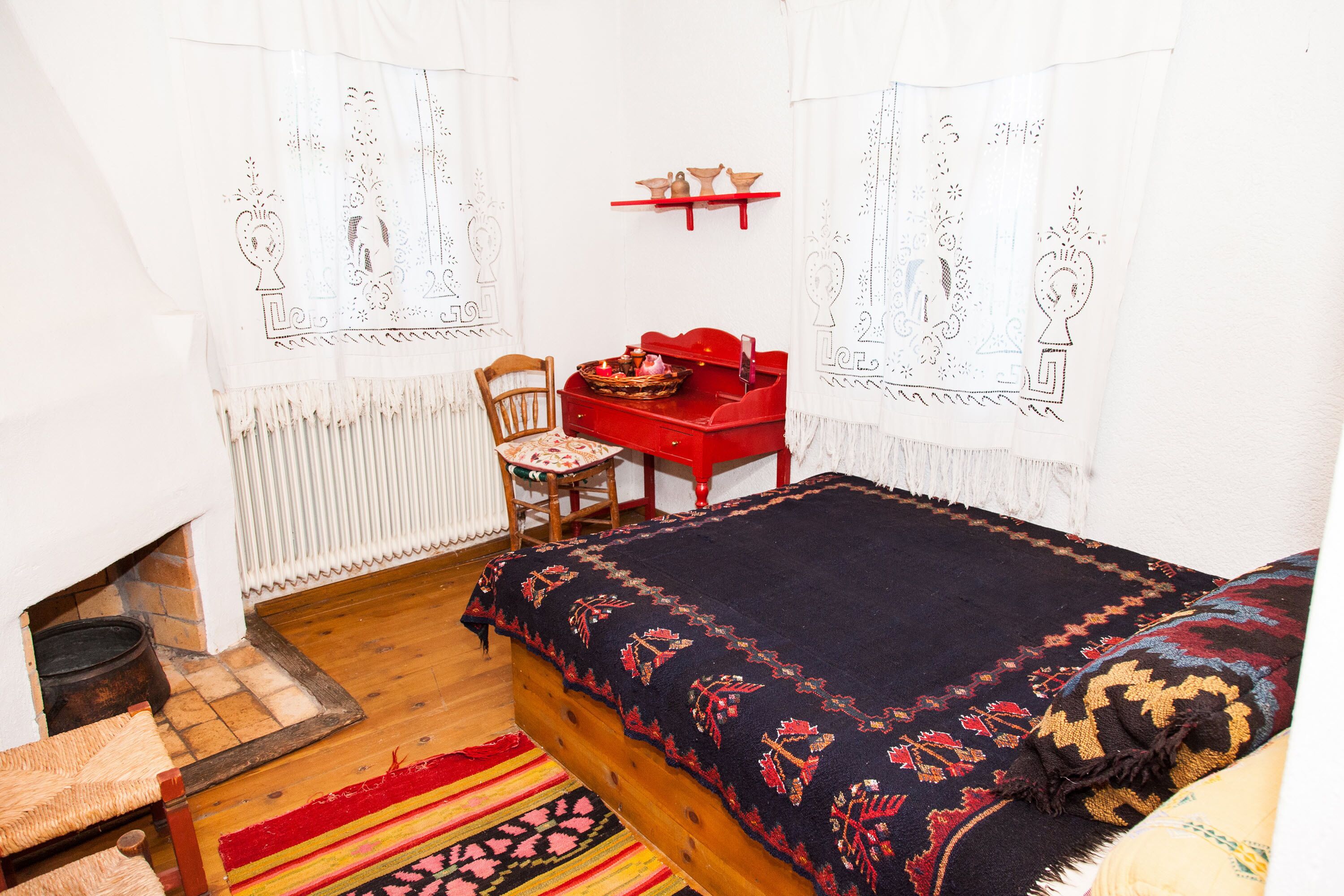 Una habitación tradicional con una cama de madera, una silla roja, una mesita y una estantería con adornos.