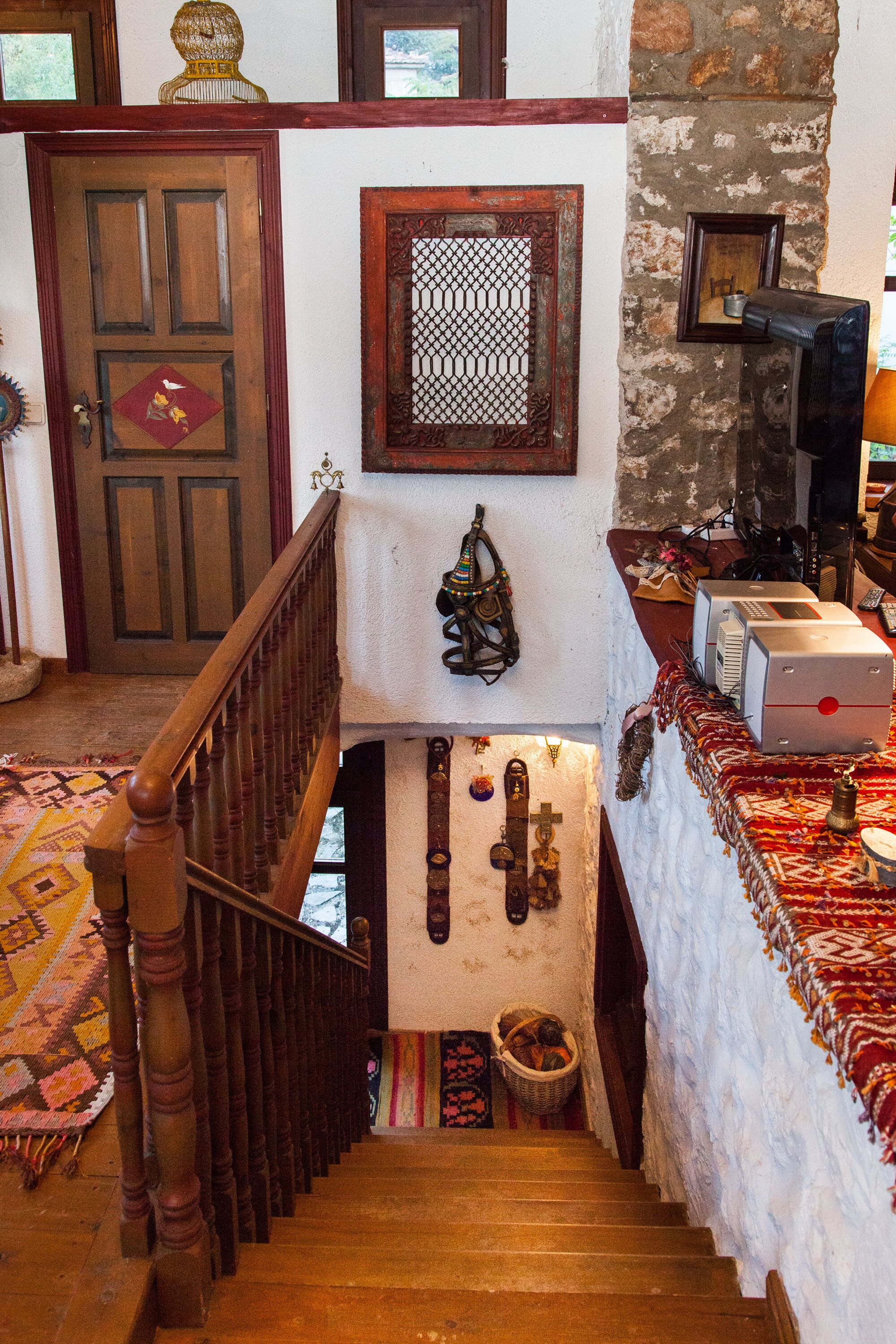 A staircase with a wooden handrail leading to a landing with a patterned rug, a basket, and a wall-mounted decorative item.