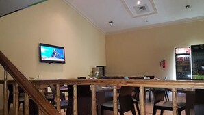 Un restaurant doté d’un bar en bois, de plusieurs tables, de chaises, d’un téléviseur fixé au mur et d’un distributeur automatique.