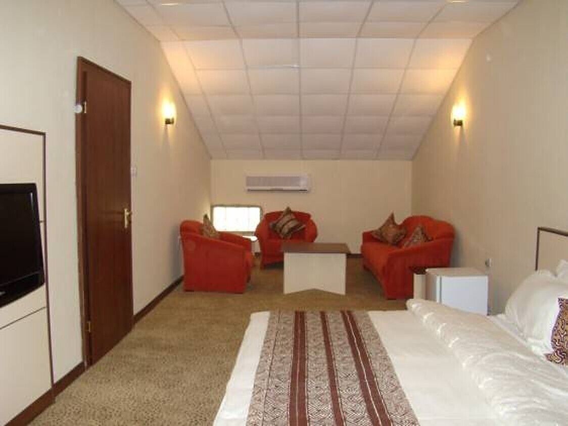 A hotel room with a bed, two red sofas, a coffee table, and a TV.