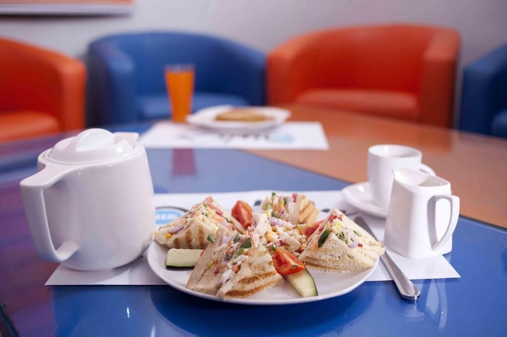 Une table mise pour le petit-déjeuner, avec une assiette de sandwichs, une carafe de lait et un verre de jus d’orange.
