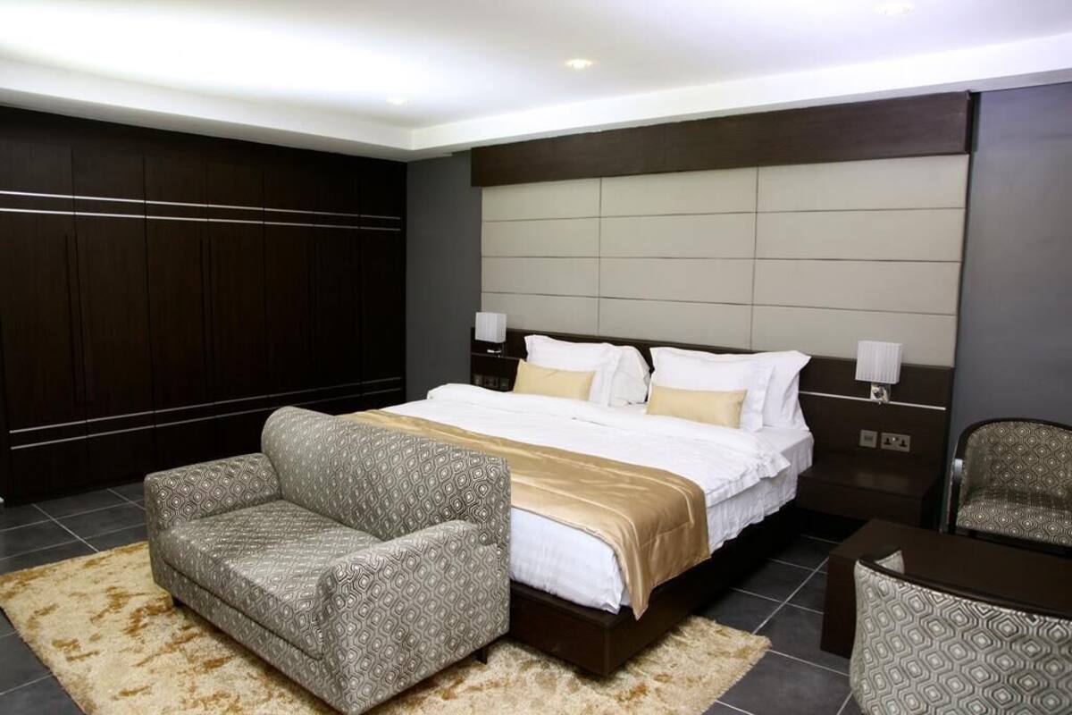A modern hotel room with a large bed, two bedside tables, a sofa, and a chair.