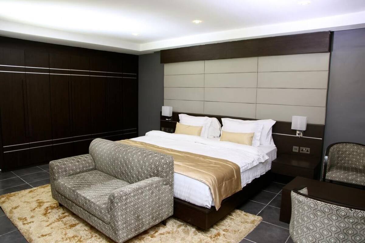 A modern hotel room with a large bed, two bedside tables, a sofa, and a chair.